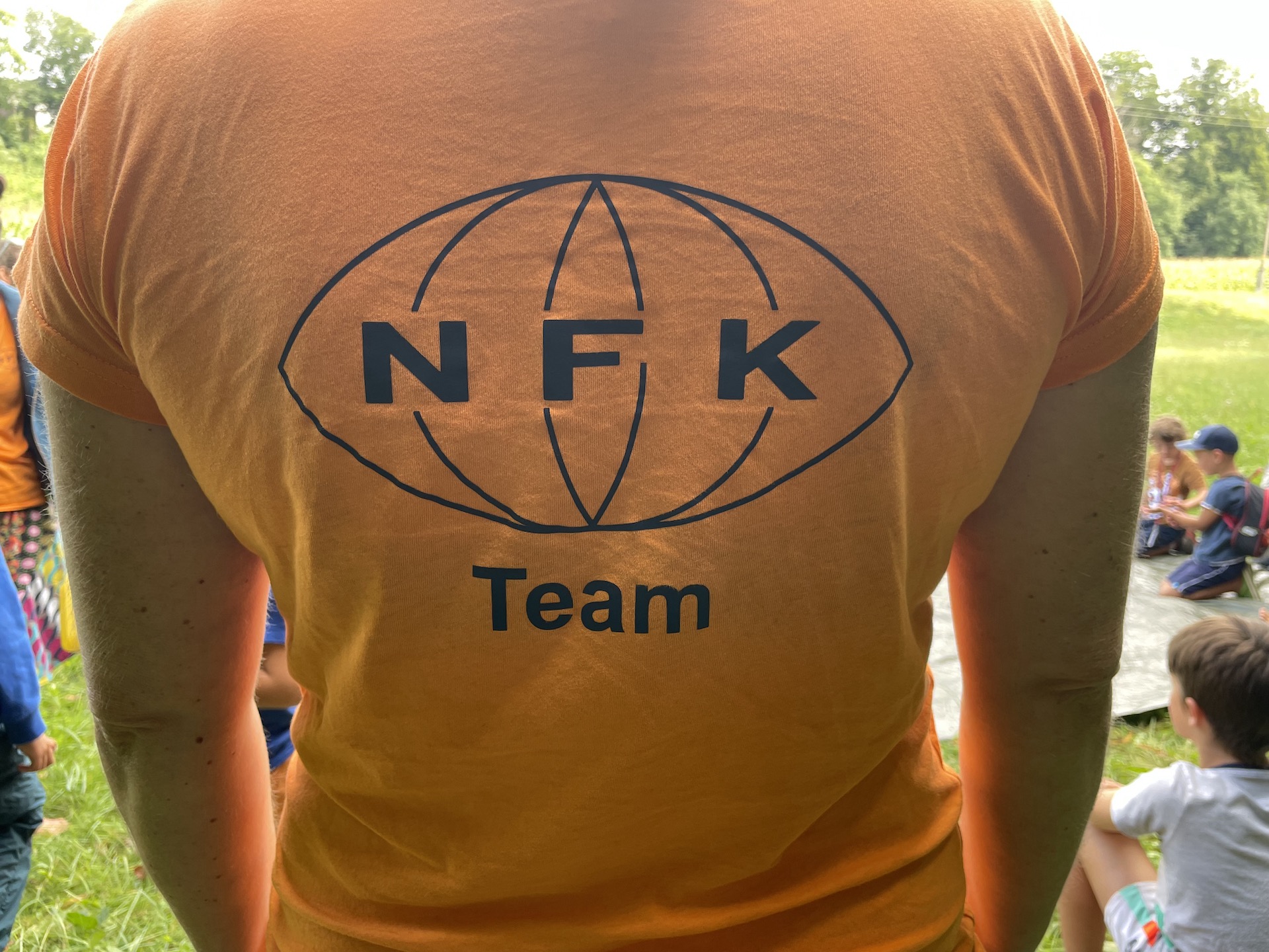 Rücken mit orangem Leiberl und Logo NFK mit der Bezeichnung Team