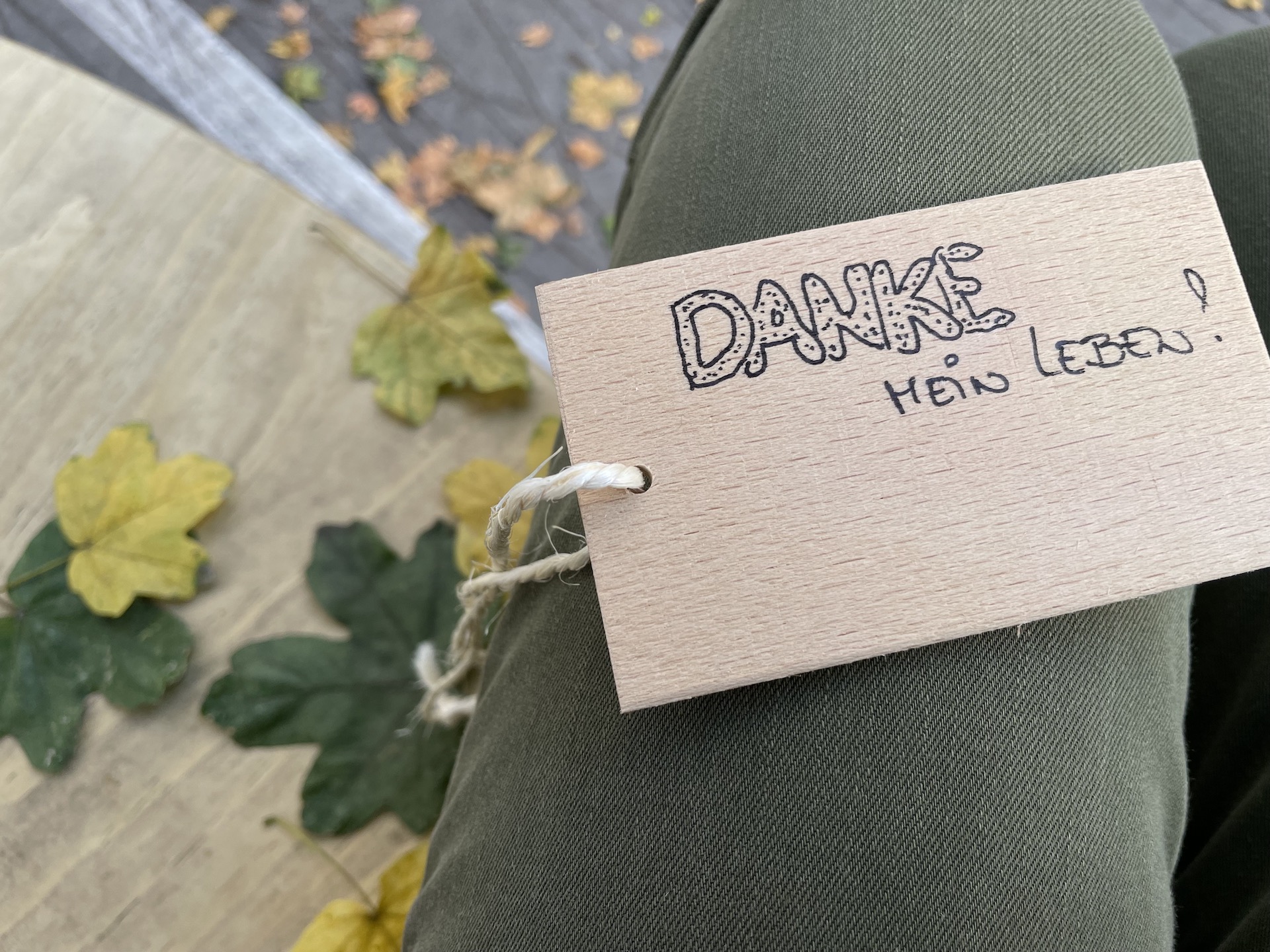 Oberschenkel, auf dem ein Holzblatt liegt darauf steht "Danke mein Leben"